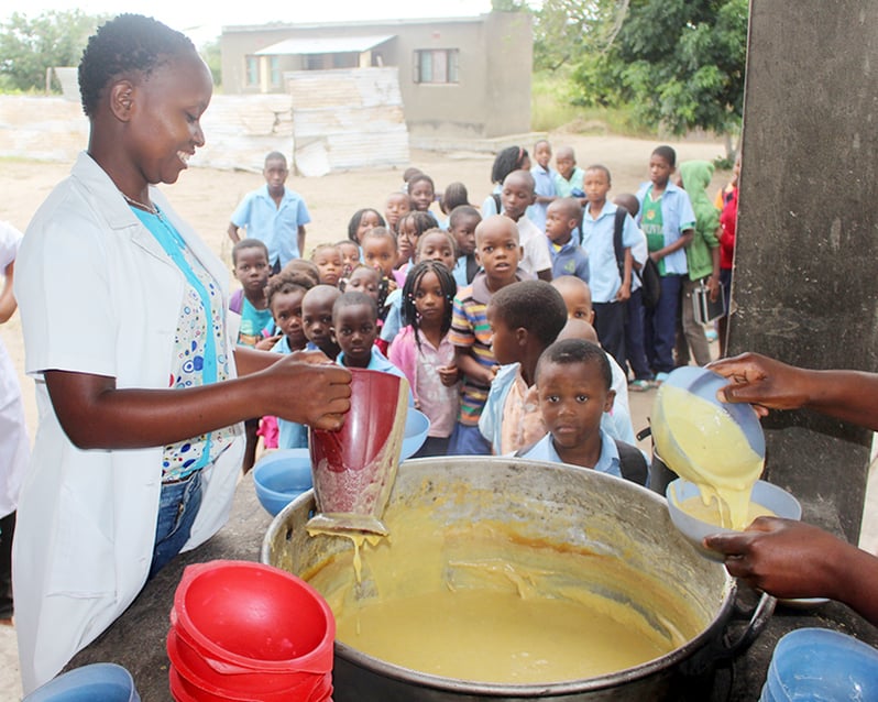 Volunteers dish out corn-soy porridge to students for lunch.