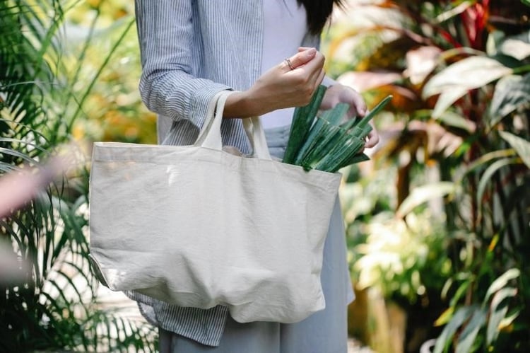 Woman holding a reusable bag in a garden.
